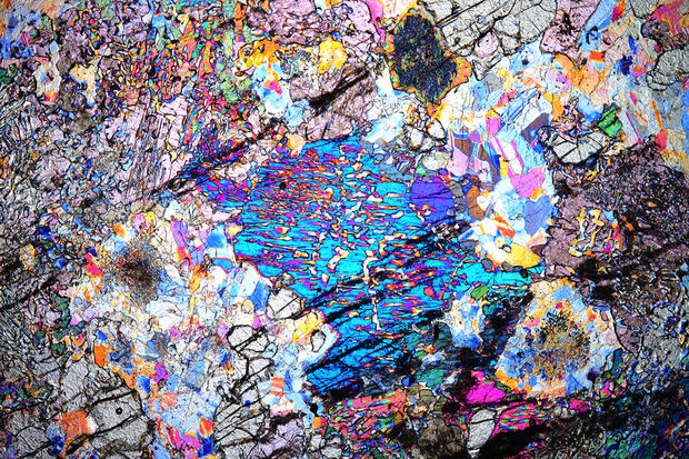 alt: Díky polarizační mikroskopii jsme schopni barevně „zviditelnit“ i jinak naprosto černé horniny pocházející ze zemského pláště. Na obrázku je modré zrno minerálu pyroxenu společně s plagioklasy, které vznikly až 100 kilometrů pod povrchem Země. Foto: Radim Jedlička.