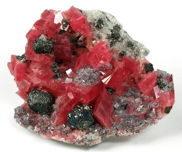 alt: Velmi hezký minerál rhodochrosit (růžovočervené krystaly) je uhličitan manganatý. Zdroj Wikimedia Commons, autor Rob Lavinsky, iRocks.com, licence CC BY-SA 3.0.